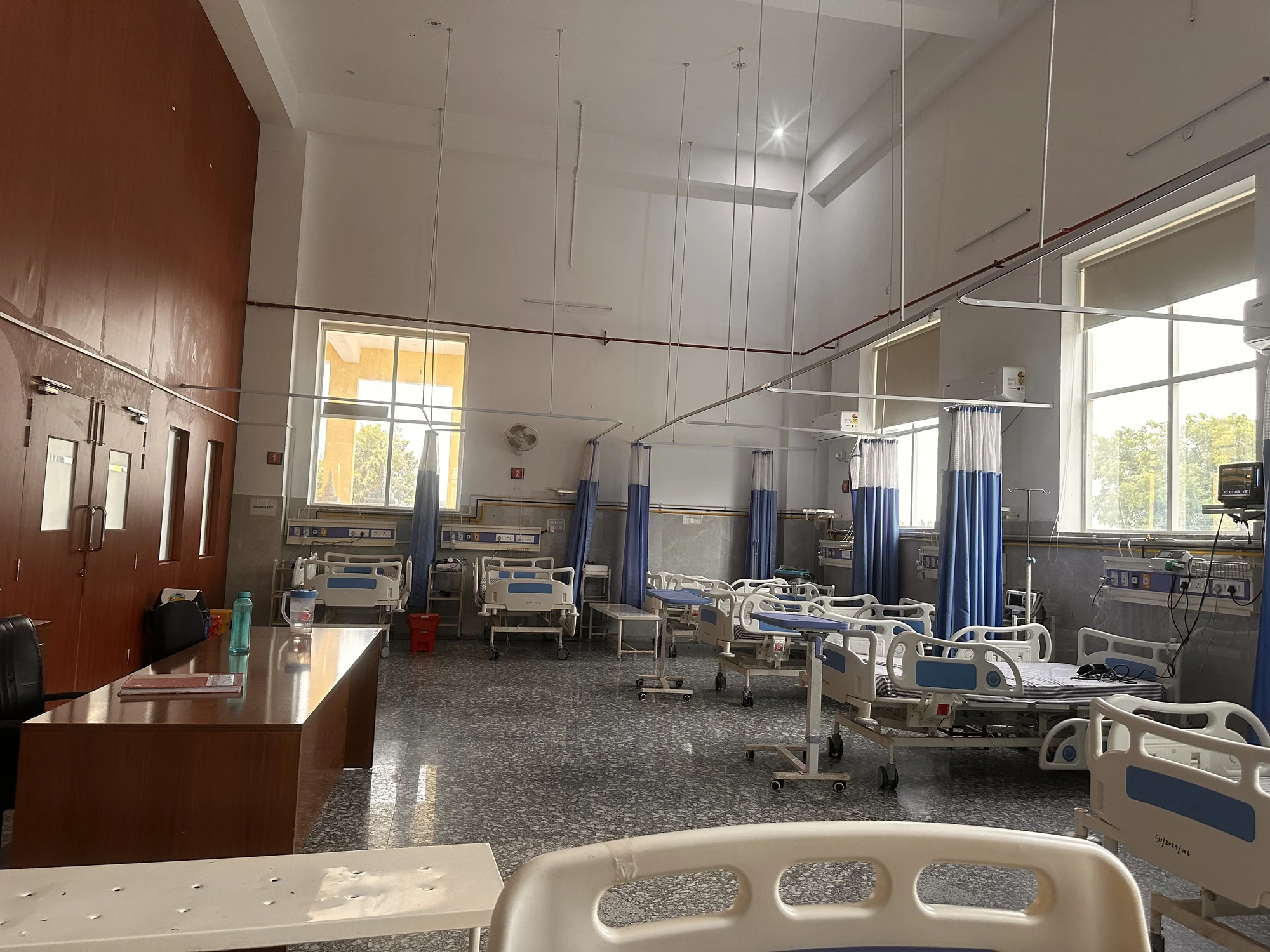 Bedded patient-care room with curtained beds and daylight from large windows